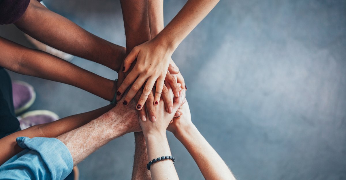 View of several people placing their hands on top of each other in support