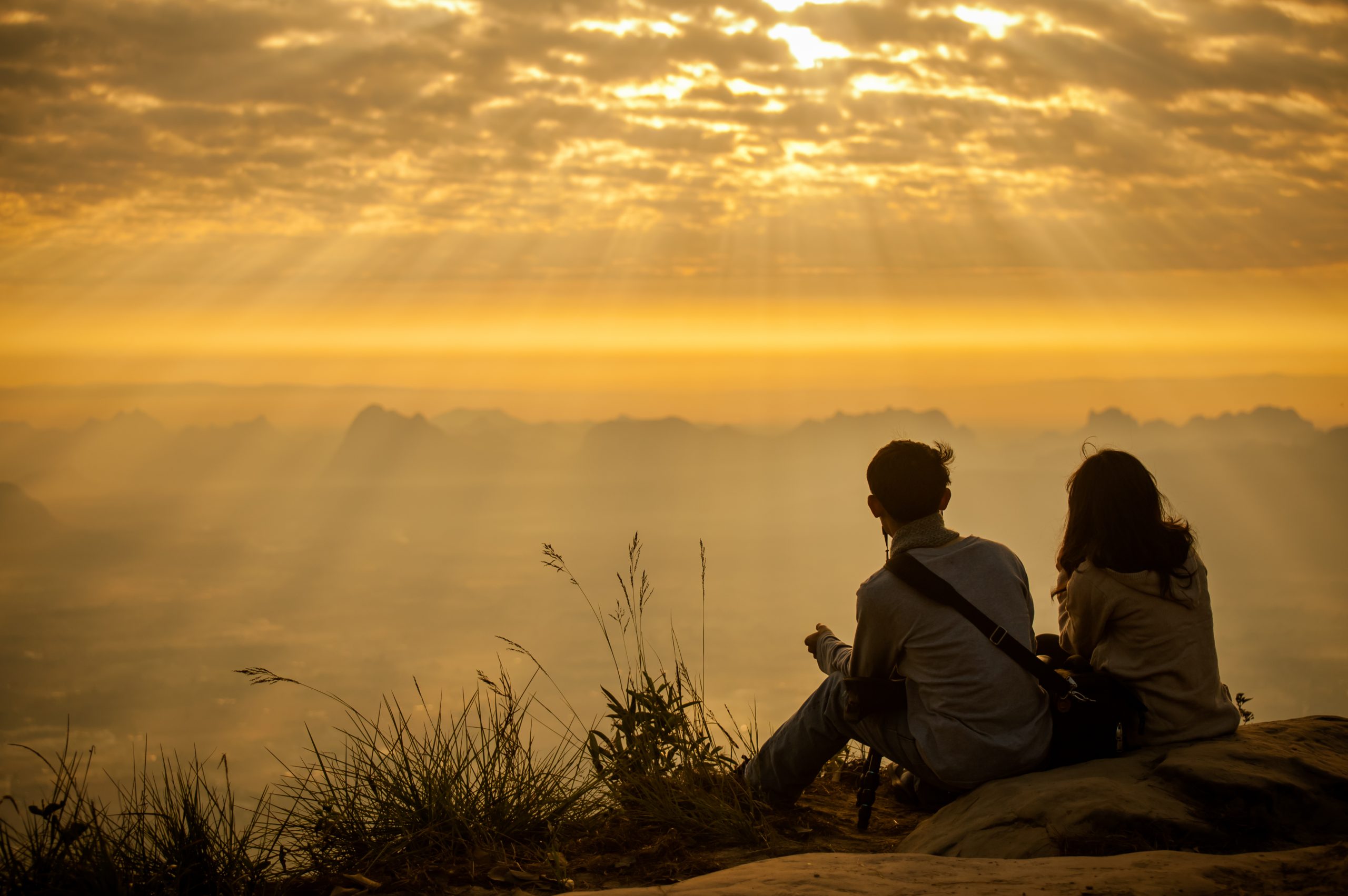 silhouette of male and female sitting on a mountain watching a sunset