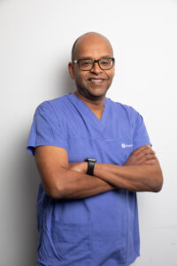 Doctor in scrubs standing with arms crossed, smiling.