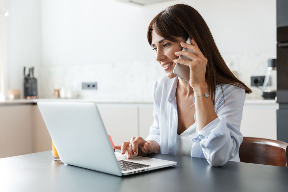 Photo,Of,A,Young,Cheerful,Happy,Woman,Indoors,At,Home woman on phone looking at computer