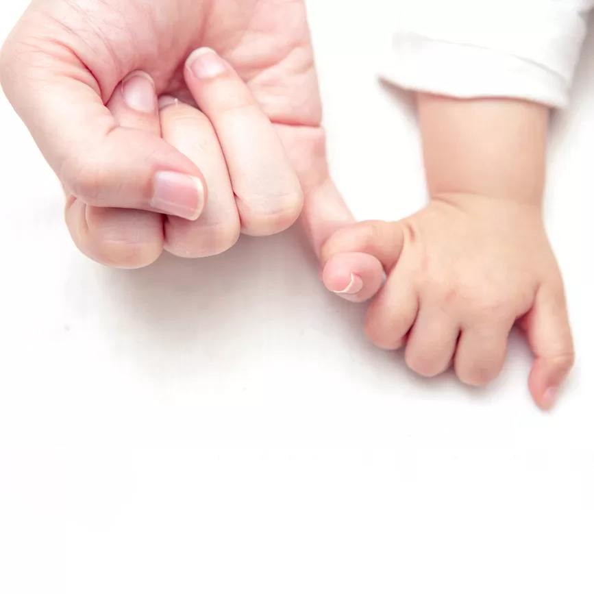 close up of a white female hand holding a tiny baby's hand against a white sheet.