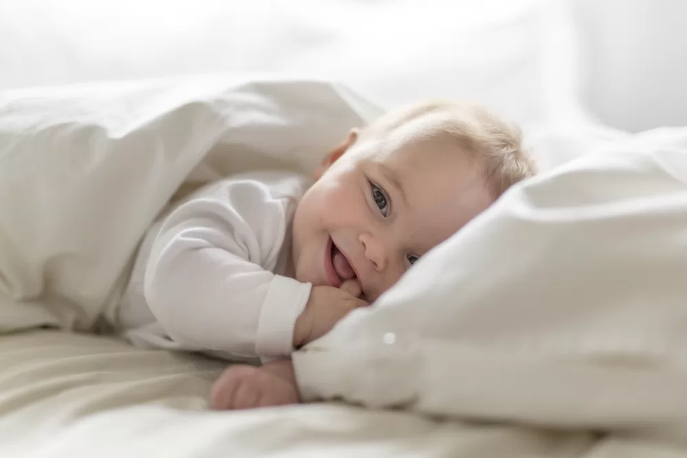 toddler dressed in white sitting on a bed smiling.