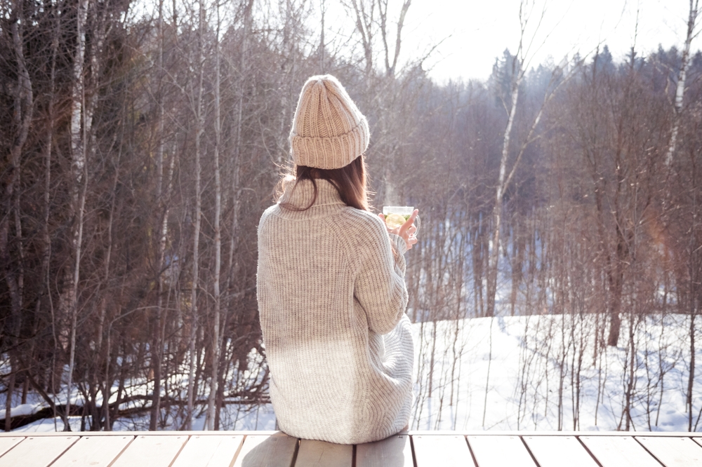 Woman sitting on a wooden step looking out into a wintery setting with trees