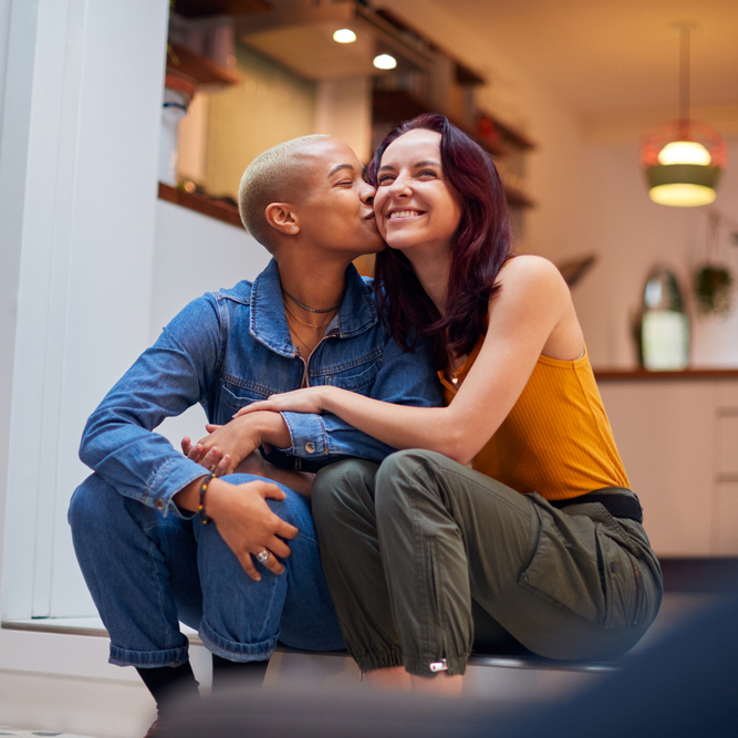 Lesbian couple sitting on a couch with one partner touching her partner's pregnant belly