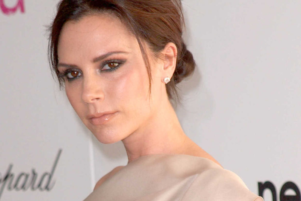 Victoria Beckham looking sideways at the camera in a beige dress.
