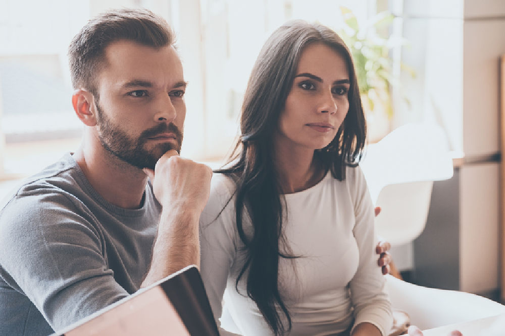 A bearded man in his 30's sits with an attractive woman in a doctor's office