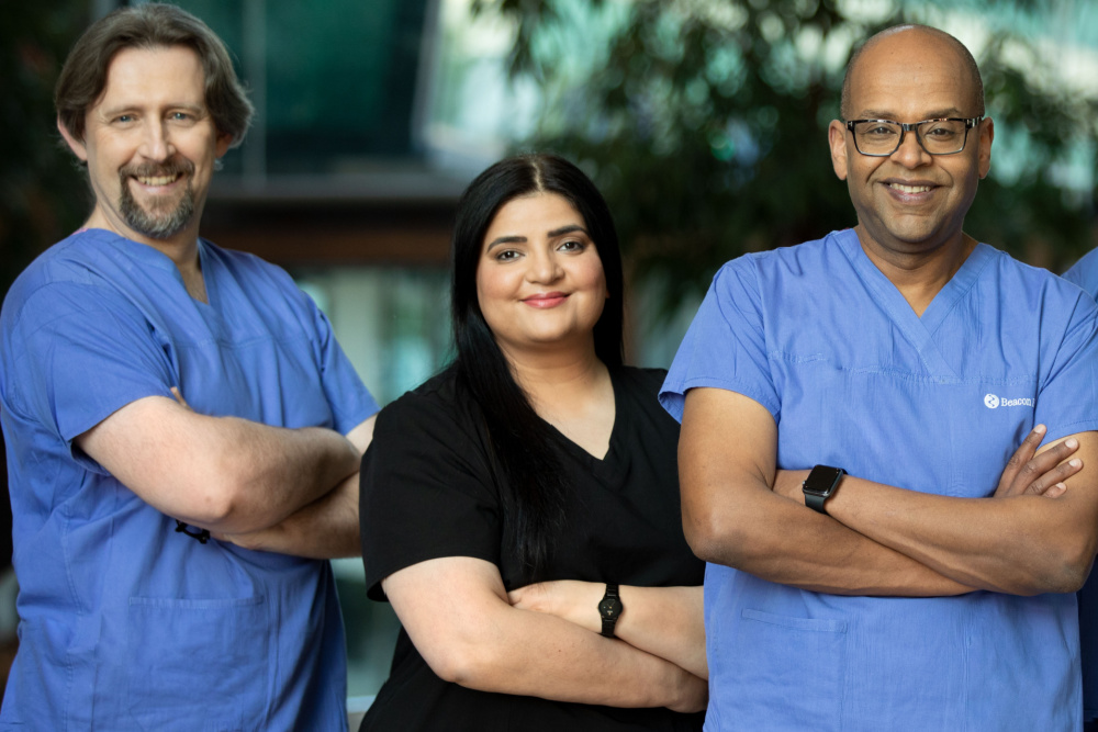 3 male doctors and one female doctor in scrubs smiling and standing with their arms crossed.