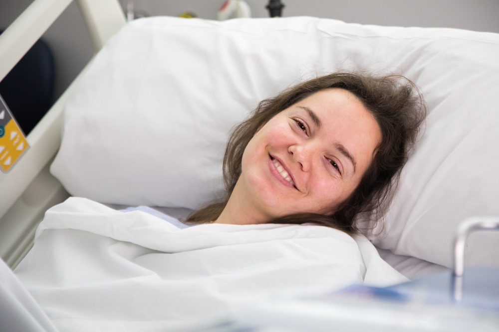 Caucasian women, 30's smiling in a hospital bed with her head on the pillow